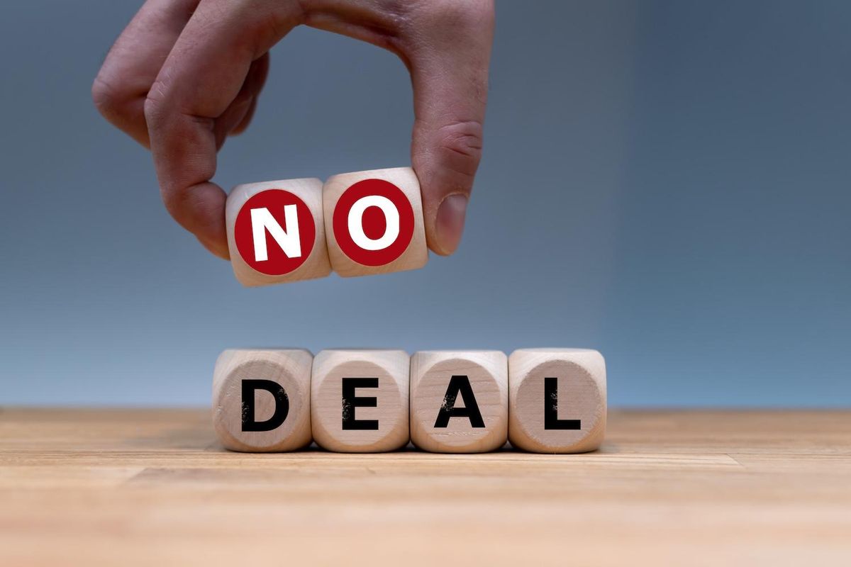 Hand rearranging letter blocks to spell "no deal" on a wooden surface.