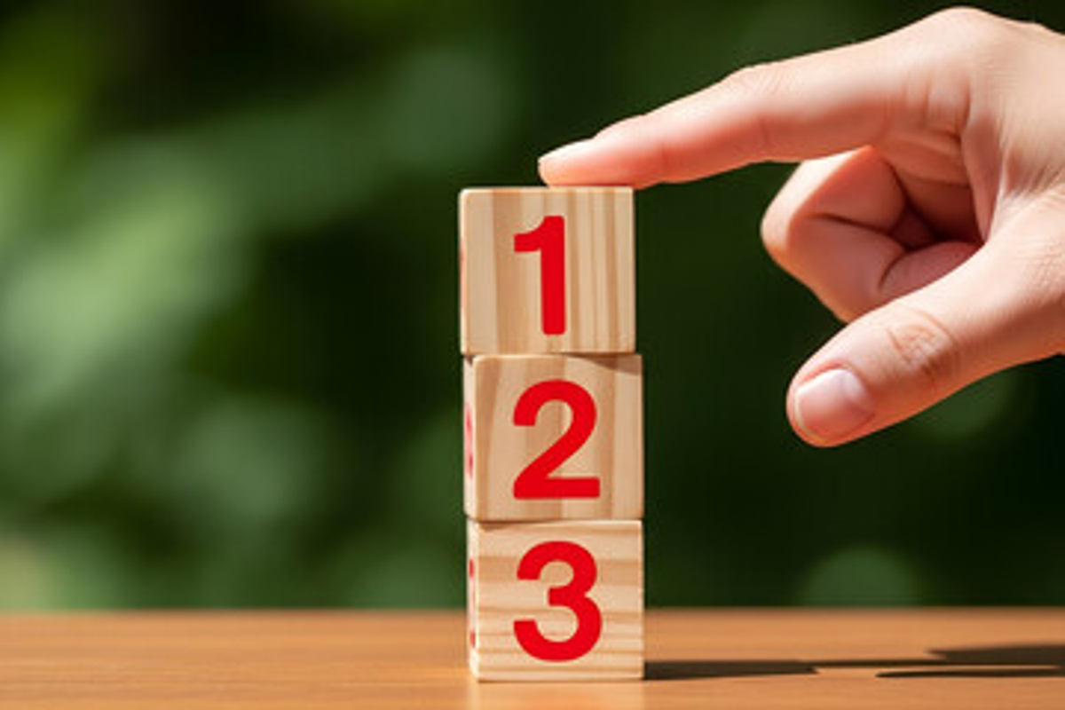 Hand stacking wooden blocks labeled 1, 2 and 3 on a table.