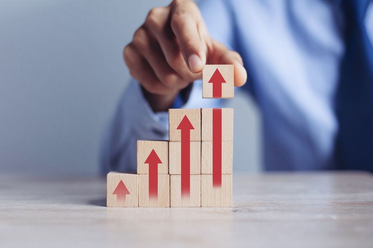 Hand stacking wooden blocks with red upward arrows, symbolizing growth.