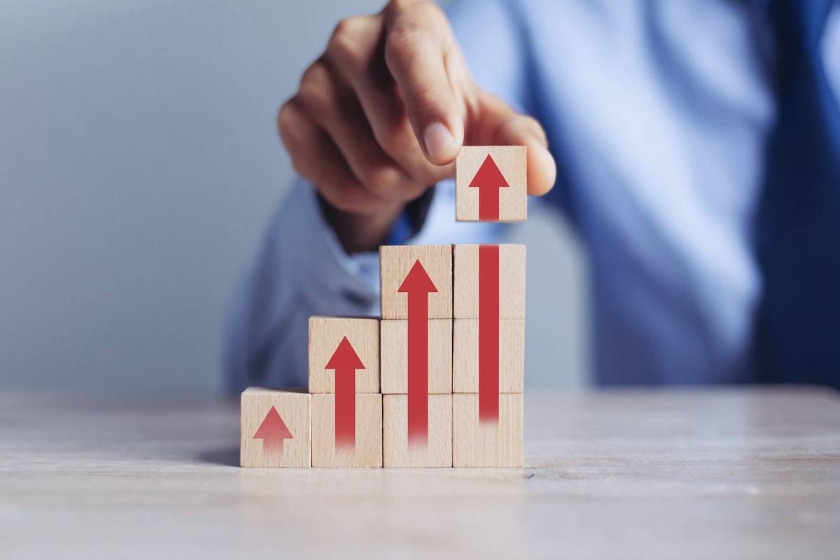 Hand stacking wooden blocks with red upward arrows, symbolizing growth.