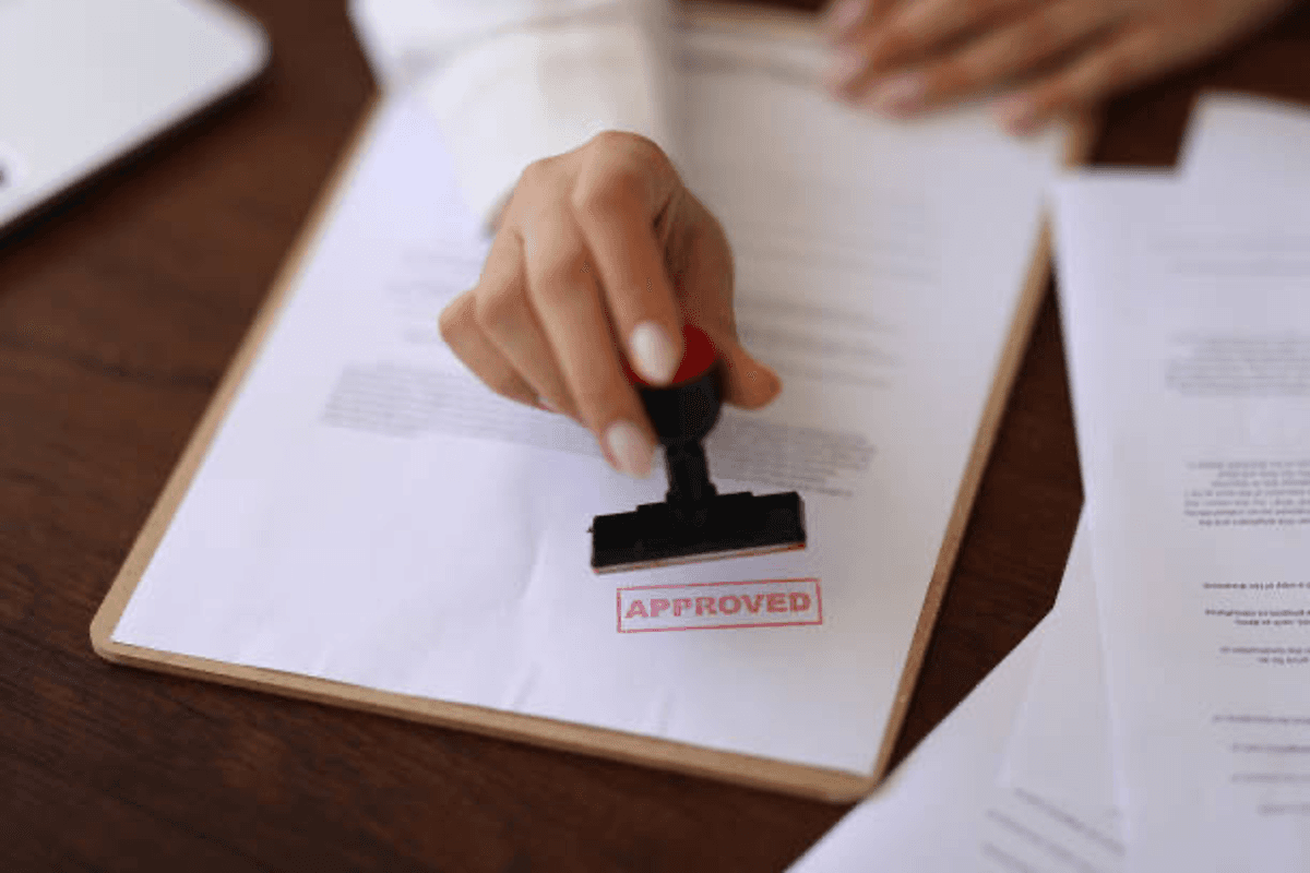 Hand stamping "approved" on a document on a clipboard.