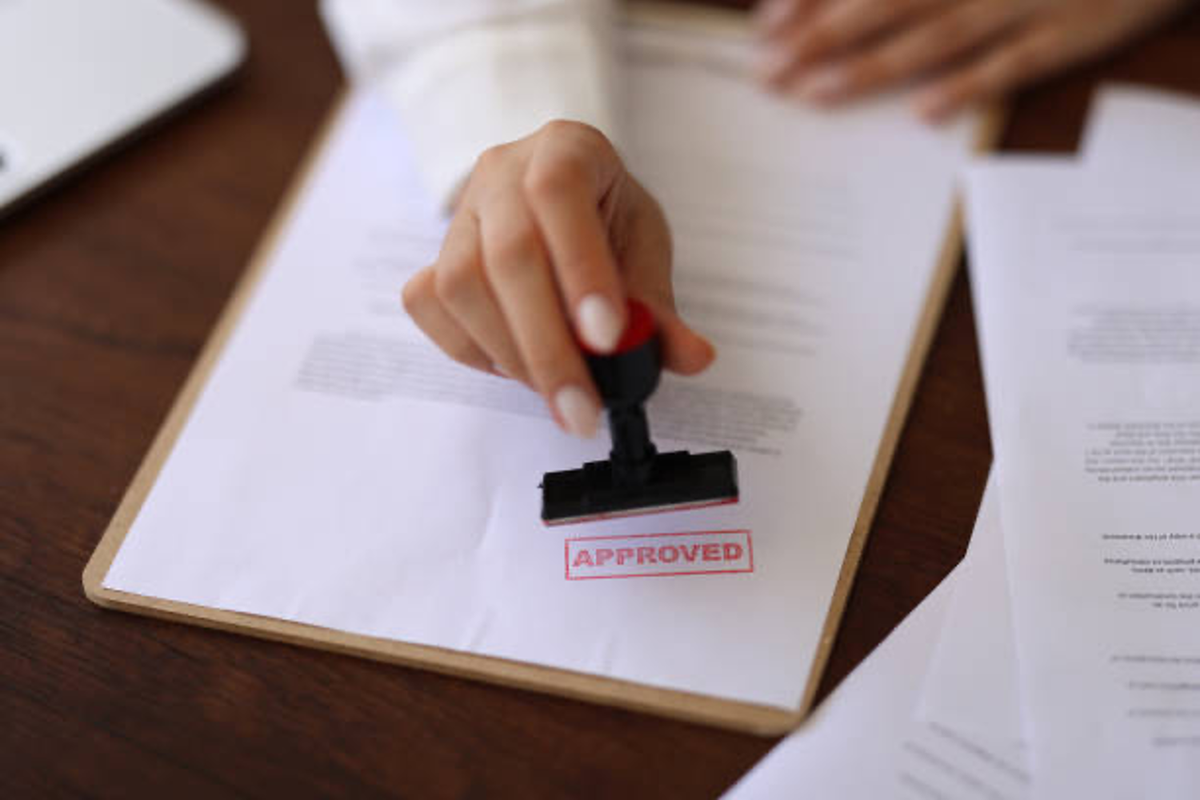 Hand stamping "approved" on a document on a clipboard.