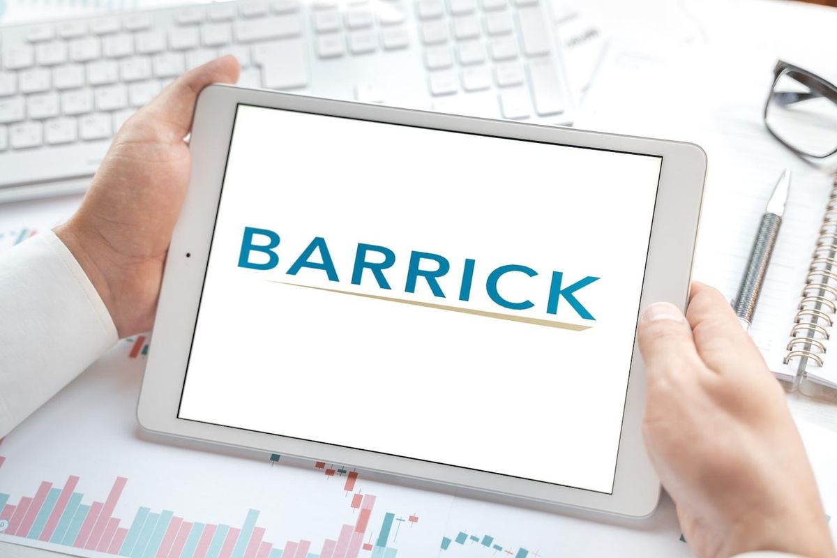 Hands holding a tablet displaying "BARRICK" logo on a desk.