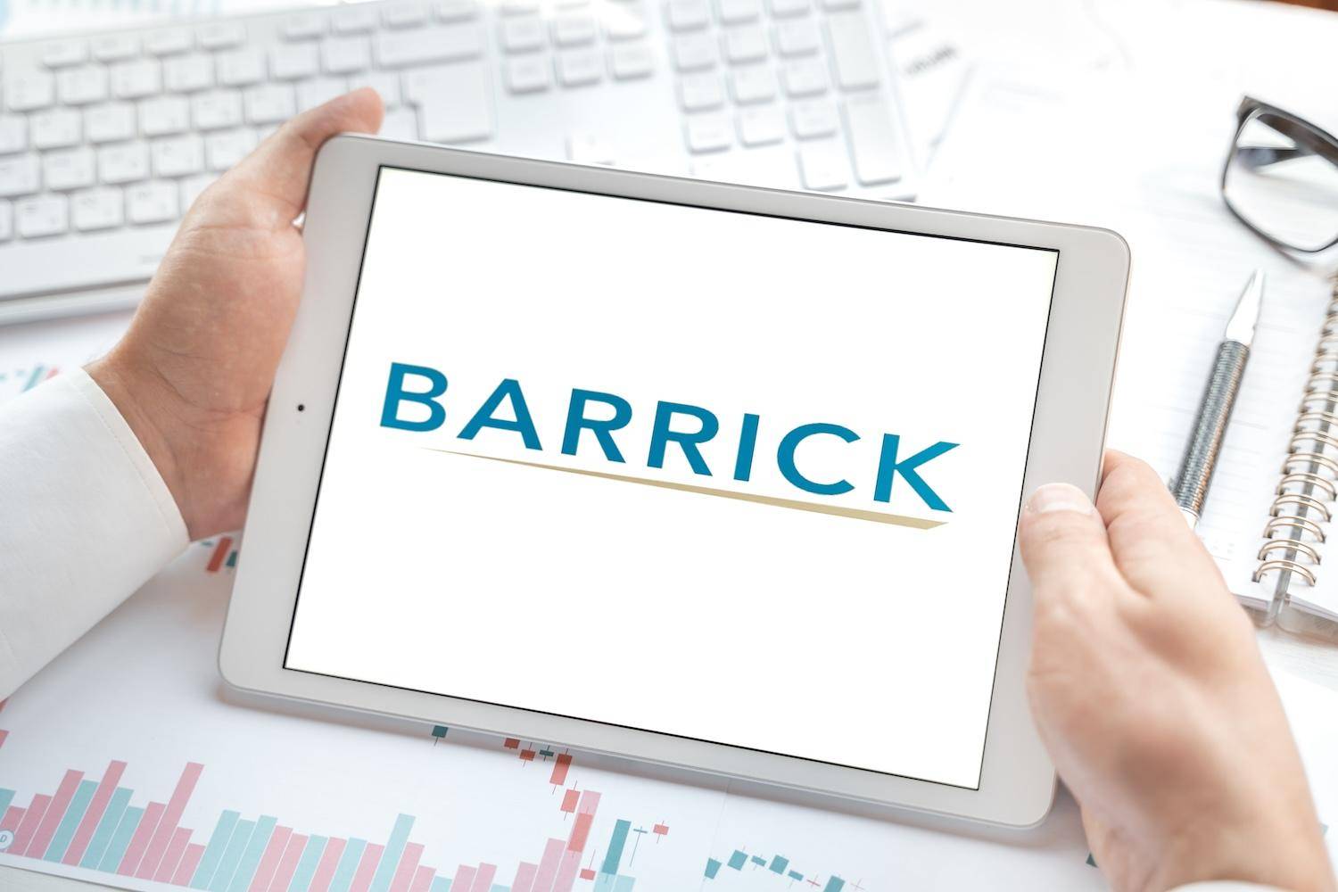 Hands holding a tablet displaying Barrick logo on a desk.