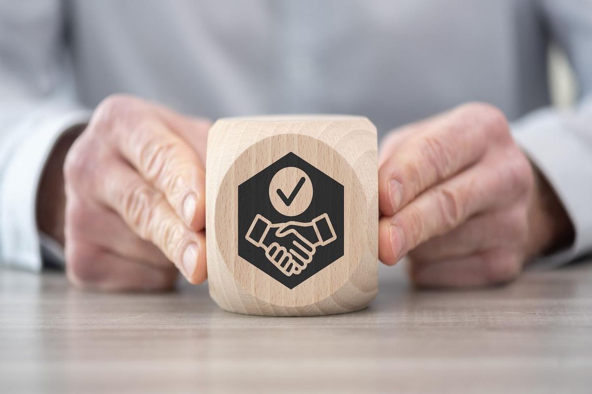 Hands holding a wooden block with a handshake and checkmark symbol.