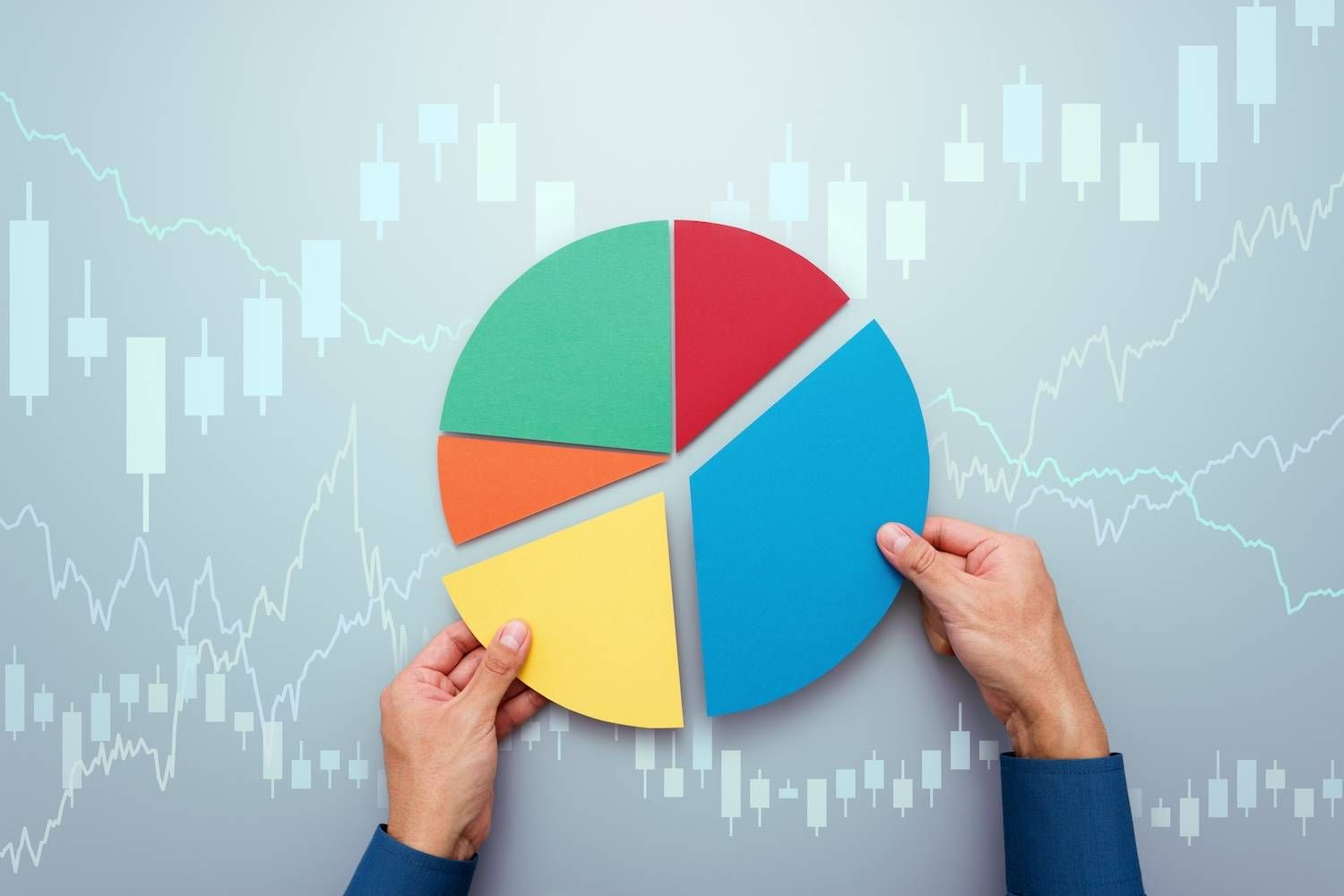 Hands holding colorful pie chart pieces over financial graphs.