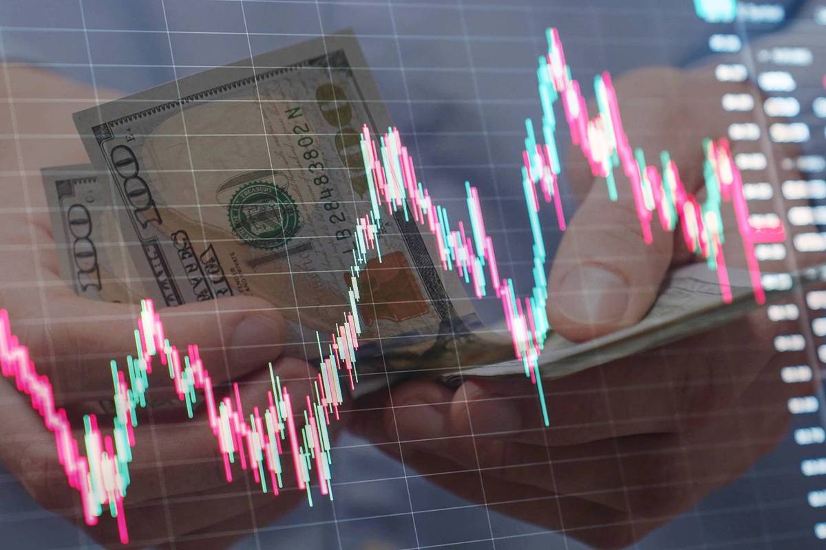 Hands holding dollar bills behind a fluctuating stock market graph with red and green candlesticks.