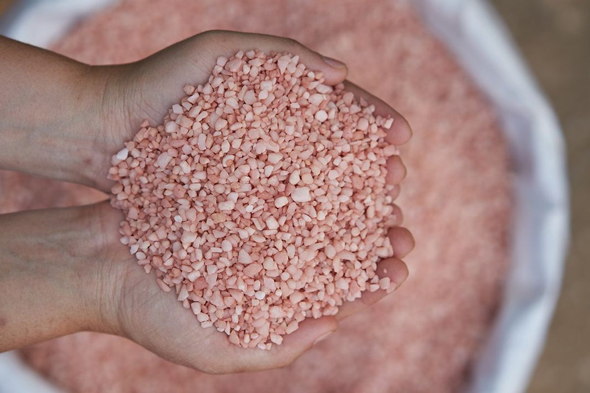 Hands holding pink rock salt over a white bag filled with more pink rock salt.