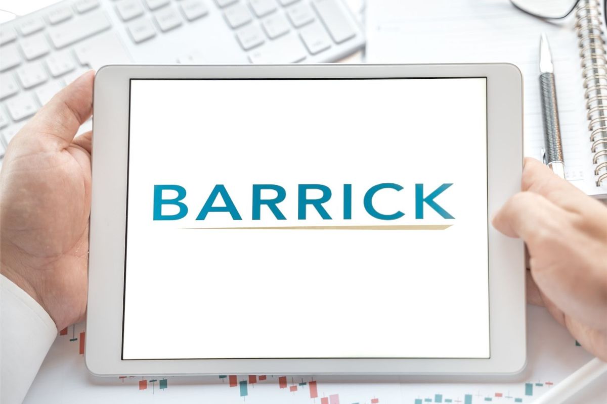 Hands holding tablet displaying Barrick logo, keyboard in the background.