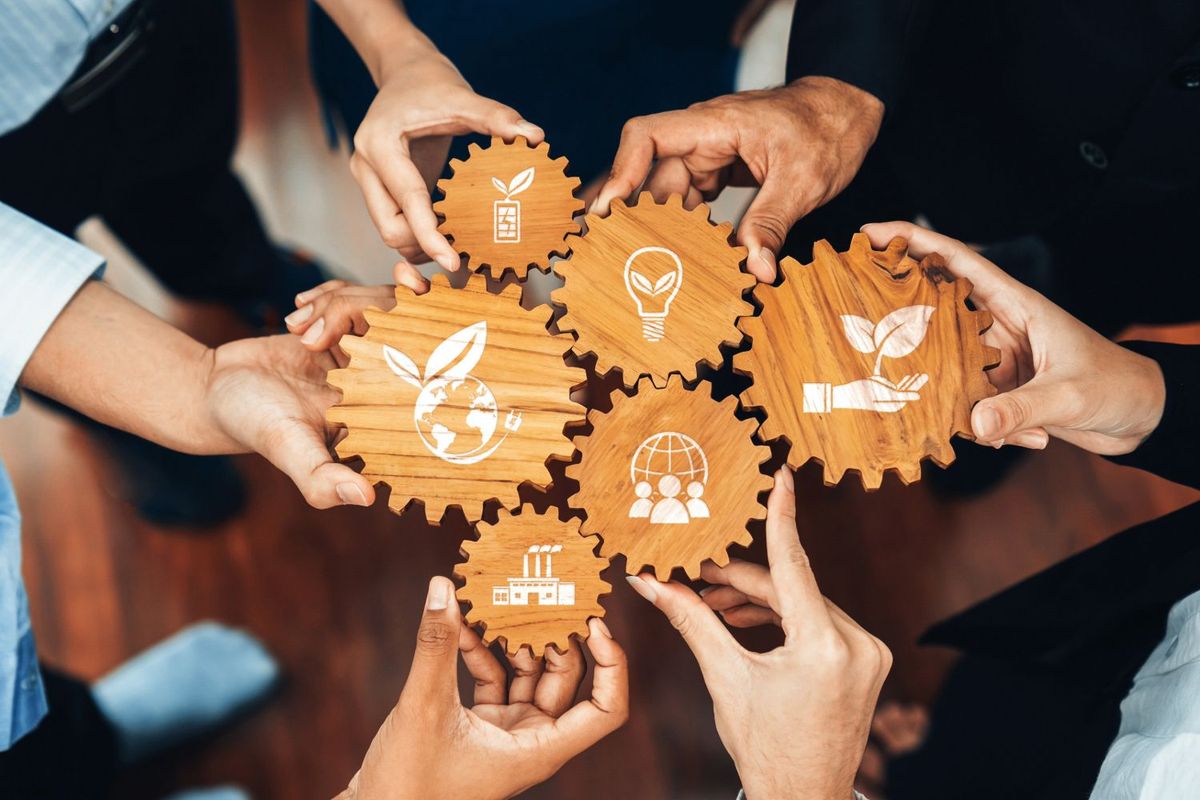 Hands holding wooden gears with sustainability icons.