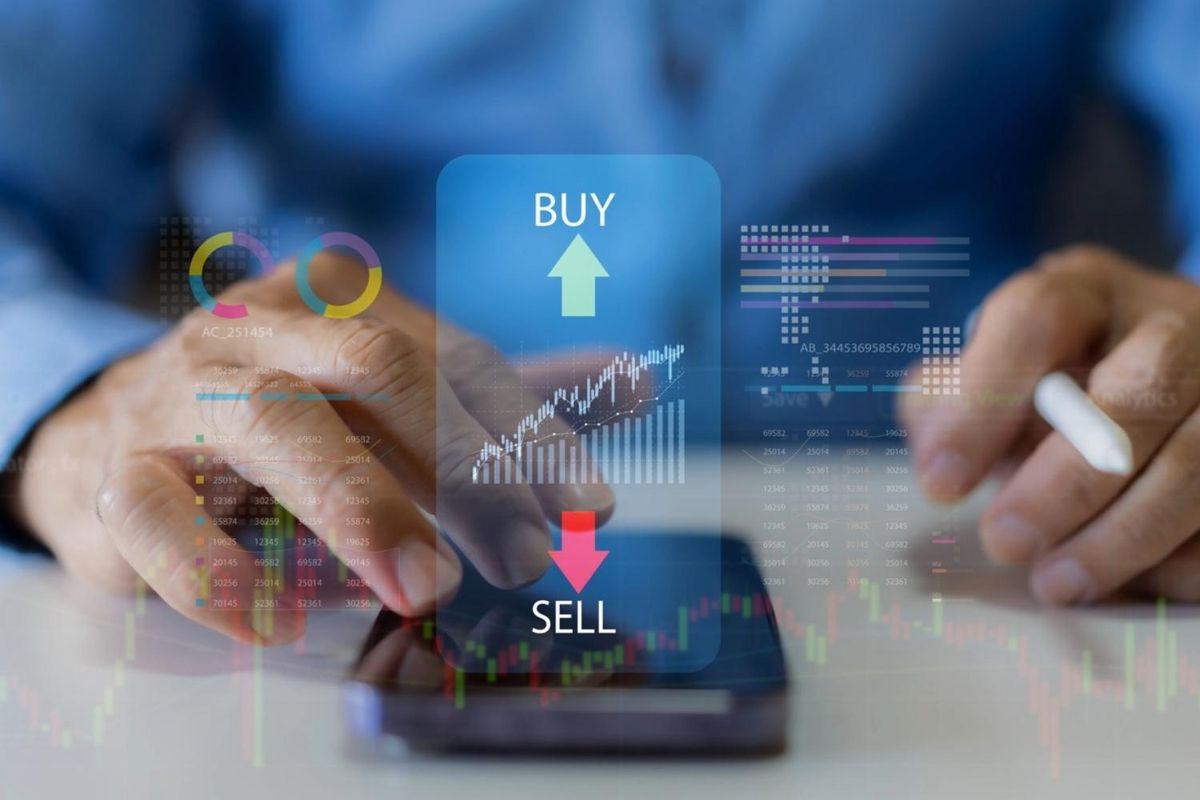 Hands using a smartphone for stock trading with "Buy" and "Sell" buttons displayed.