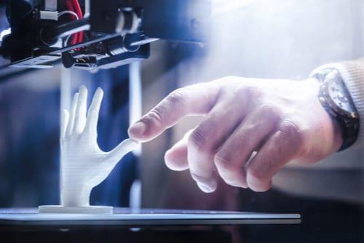 human hand touching 3D printed hand in 3D printer