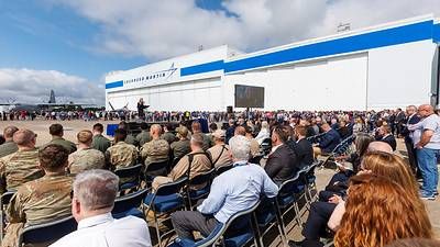 Trish Pagan, vice president of Lockheed Martin's Air Mobility and Maritime Missions and general manager Marietta site, addresses guests celebrating the 75th anniversary of Lockheed Martin's Marietta manufacturing facility. In the background, Lockheed Martin employees line up to see the iconic C-130J Hercules and 5th Generation Fighter F-22 Raptor, both made in Marietta.