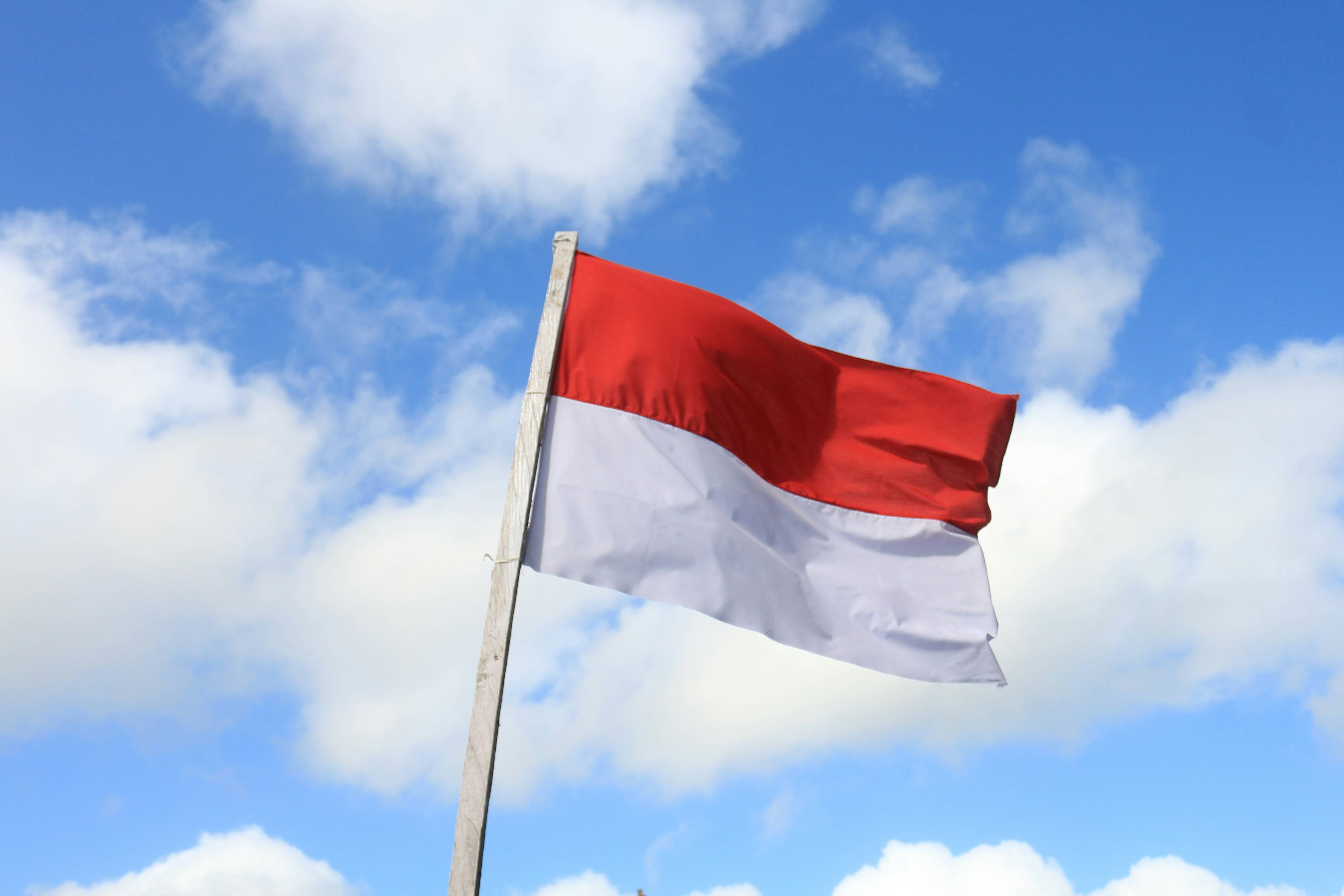 Indonesia flag flutters on a pole against a backdrop of blue sky with white clouds.