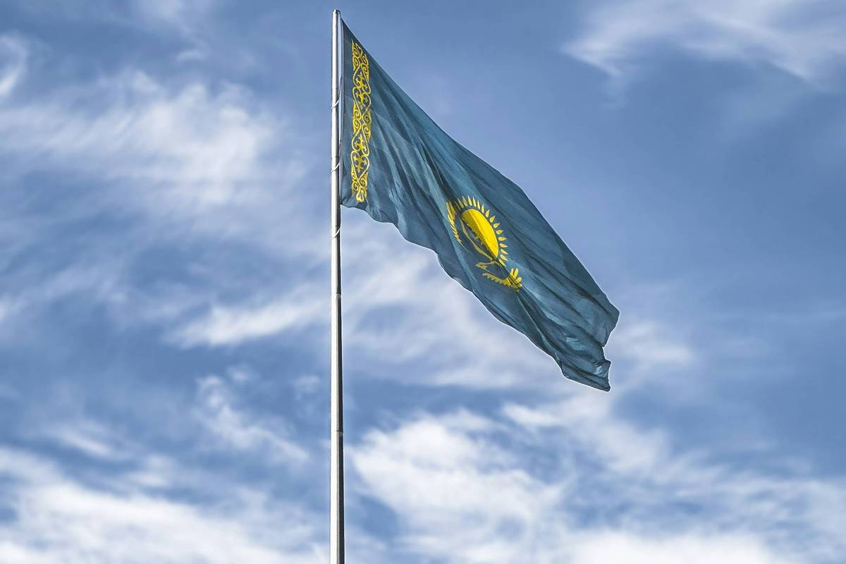 Kazakhstan flag waving against a cloudy blue sky.