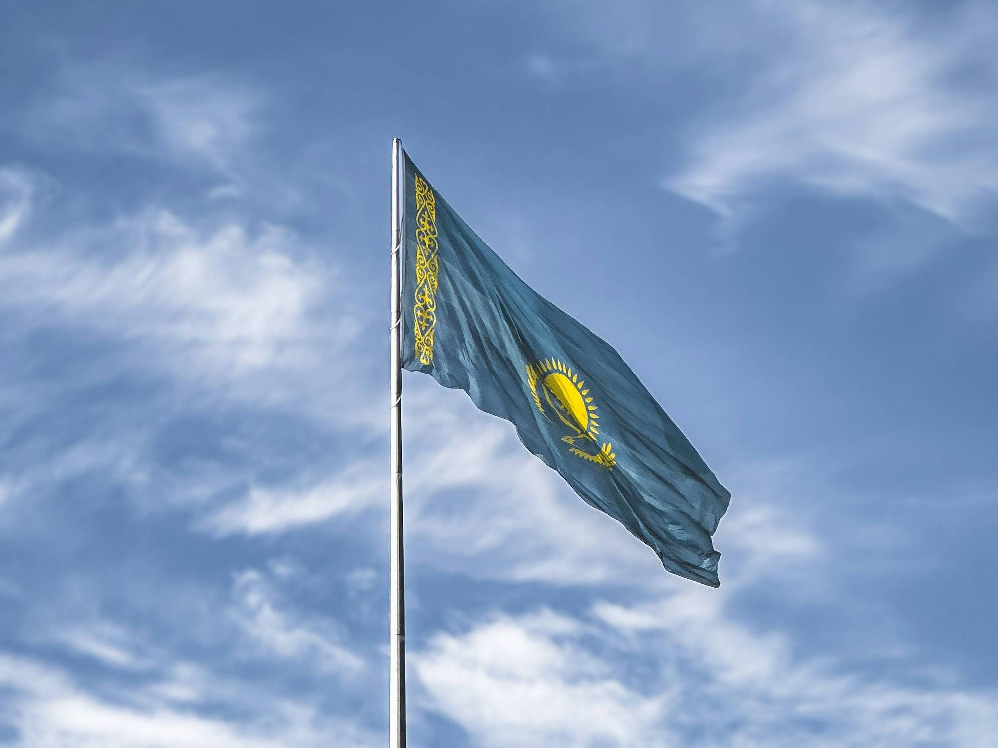 Kazakhstan flag waving against a cloudy blue sky.