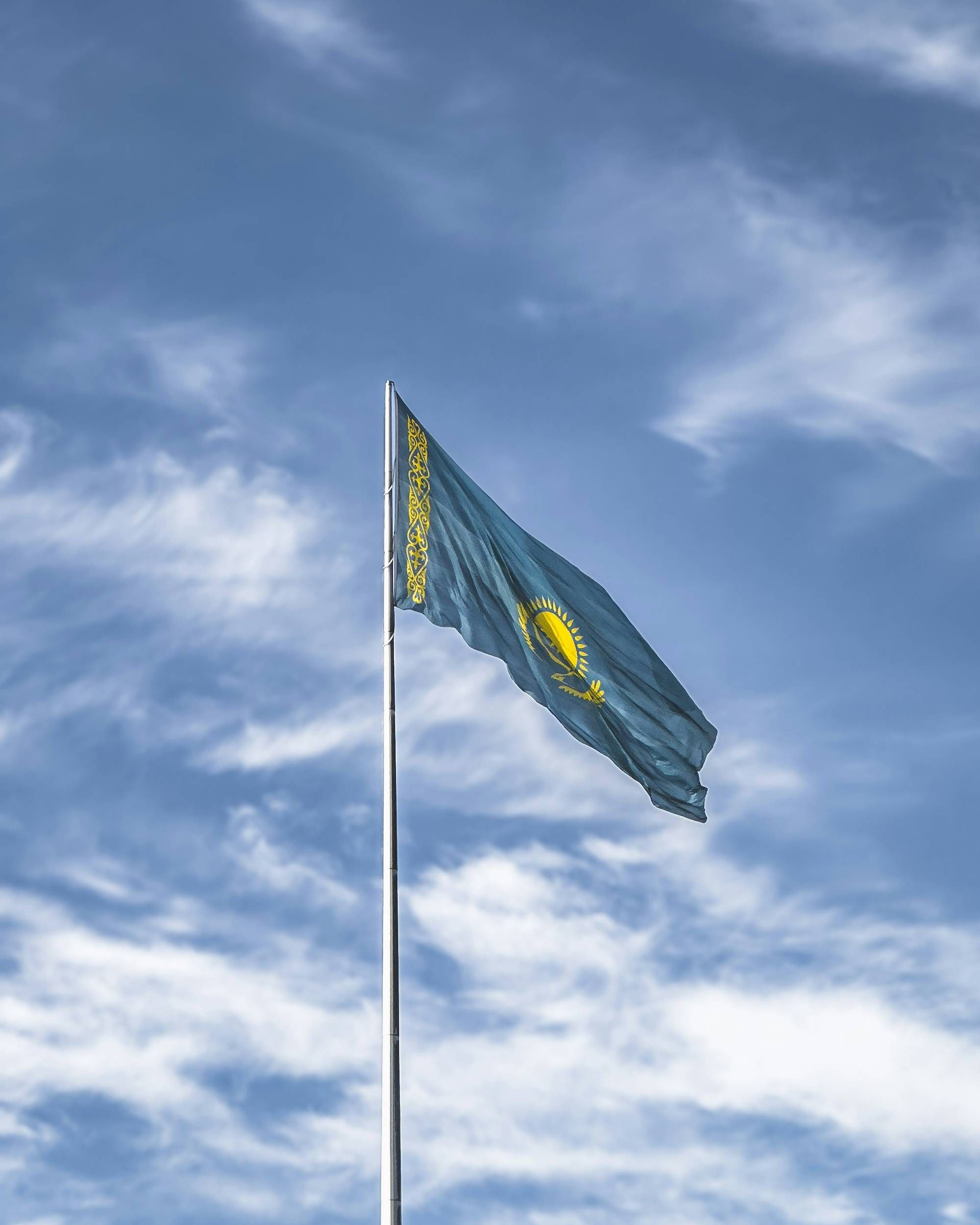 Kazakhstan flag waving against a cloudy blue sky.
