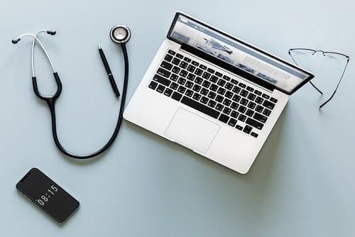 laptop, stethoscope, smartphone, pen and eyeglasses on desk