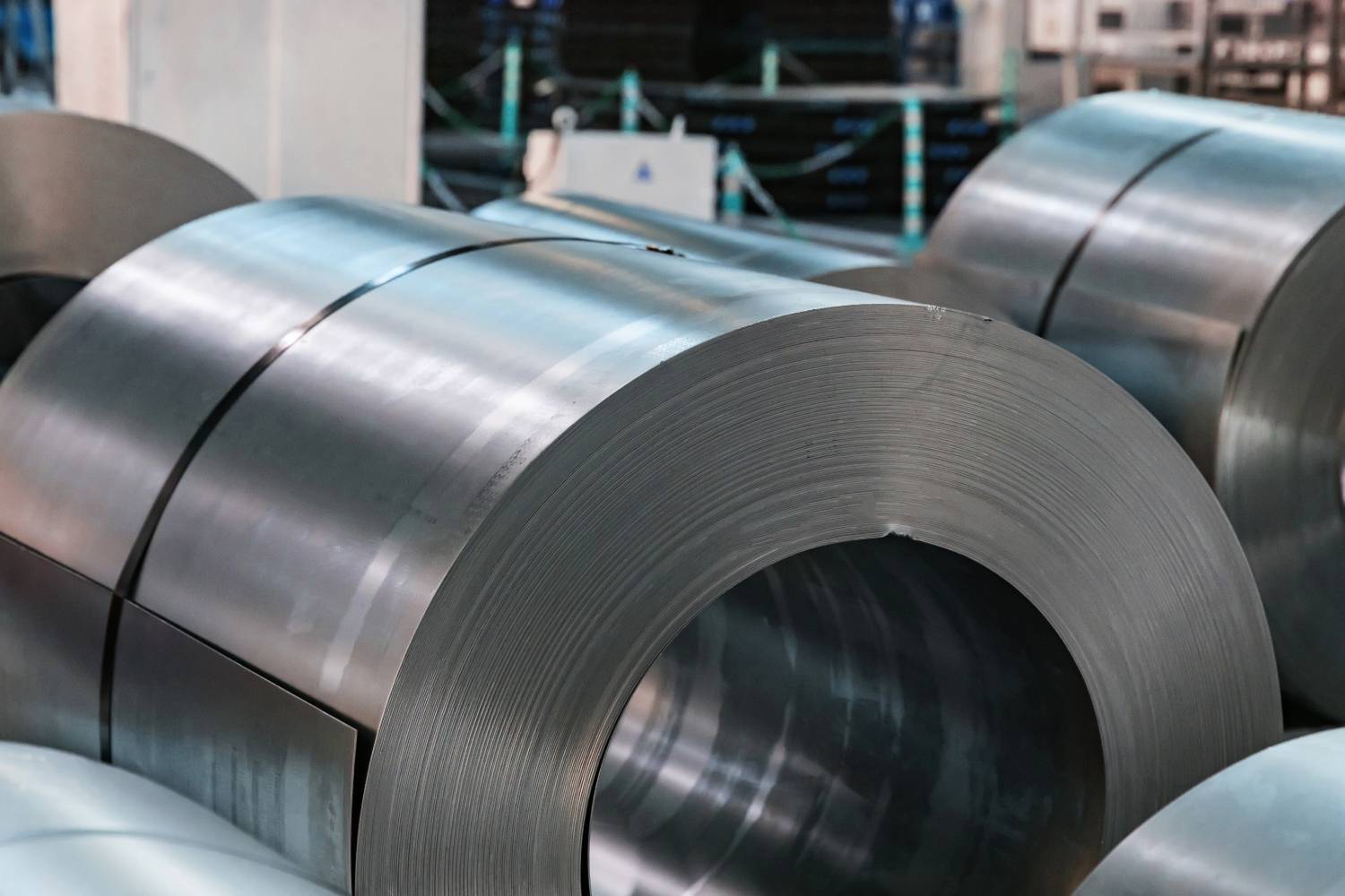 Large nickel coils with shiny silver surfaces are stacked in an industrial warehouse setting.