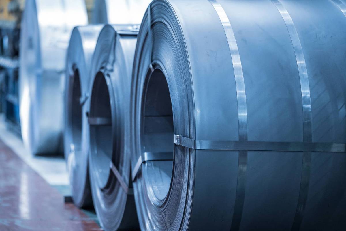 Large steel coils lined up in factory with shiny metal straps over smooth surface.