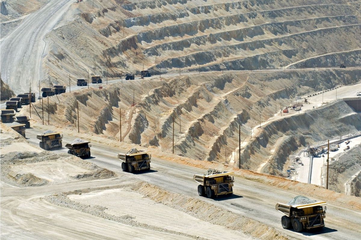 Line of dump trucks moving ore at open-pit mine.