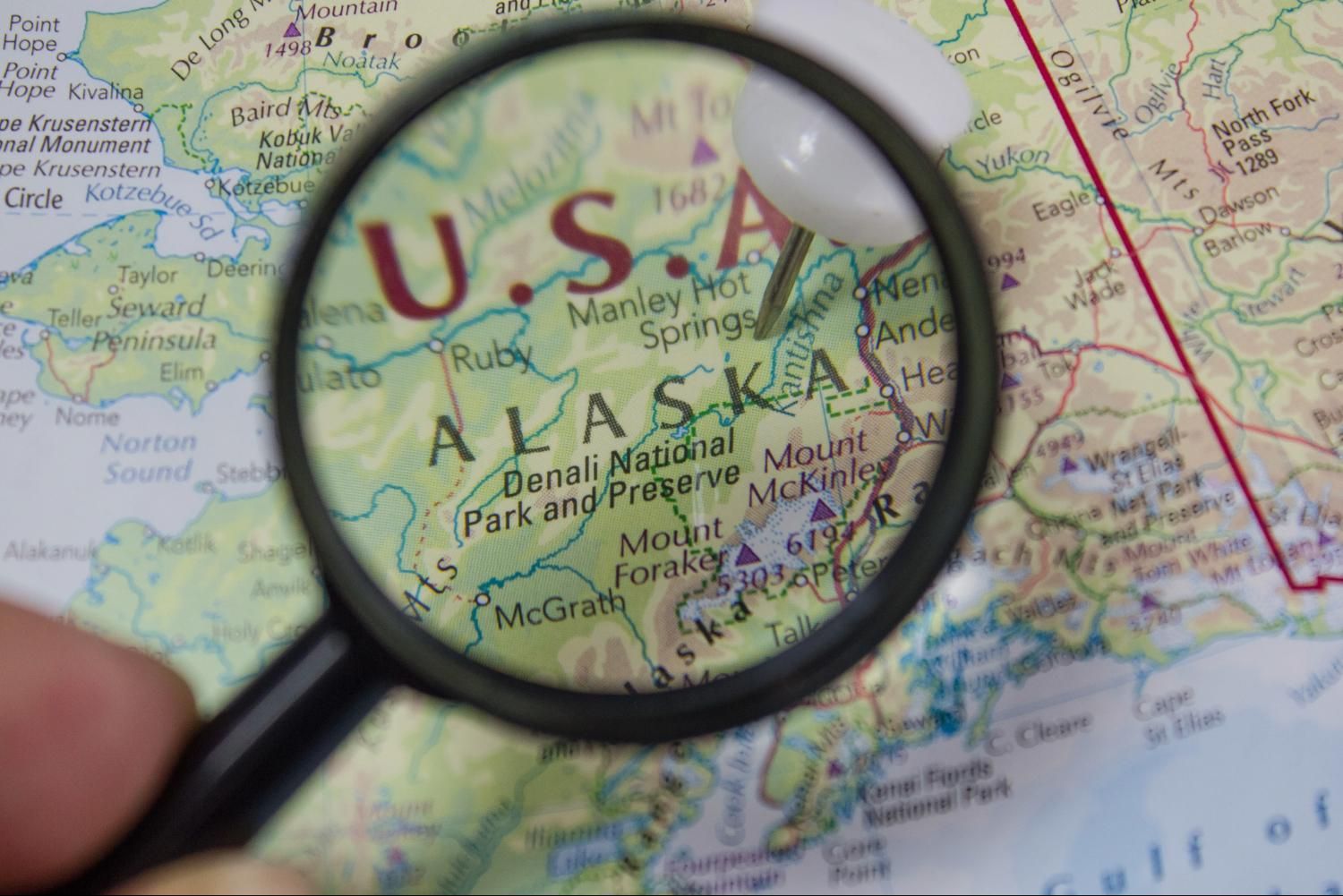 Magnifying glass highlighting Alaska on a detailed US map.