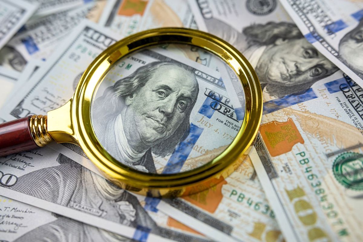 Magnifying glass over a stack of US $100 bills.