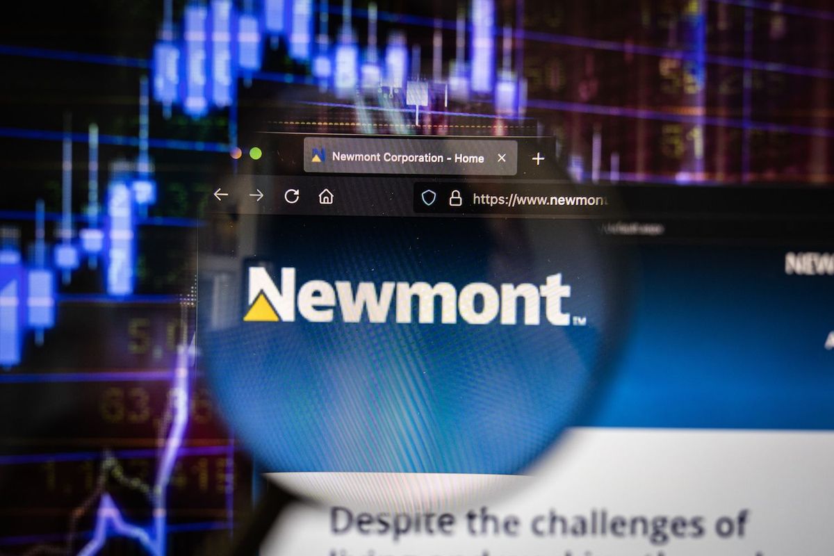 Magnifying glass over Newmont's website with financial charts in the background.