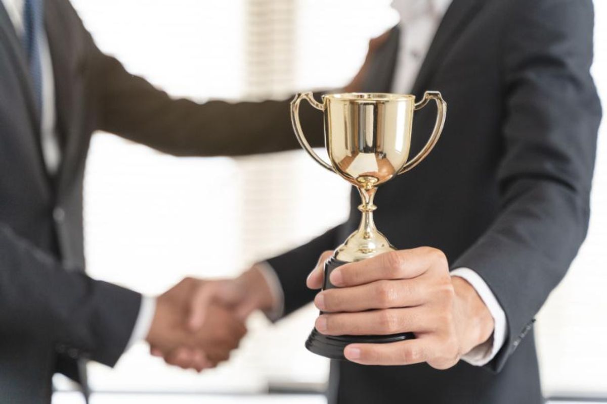 man holds trophy in left and hand and uses right hand to shake another person's hands