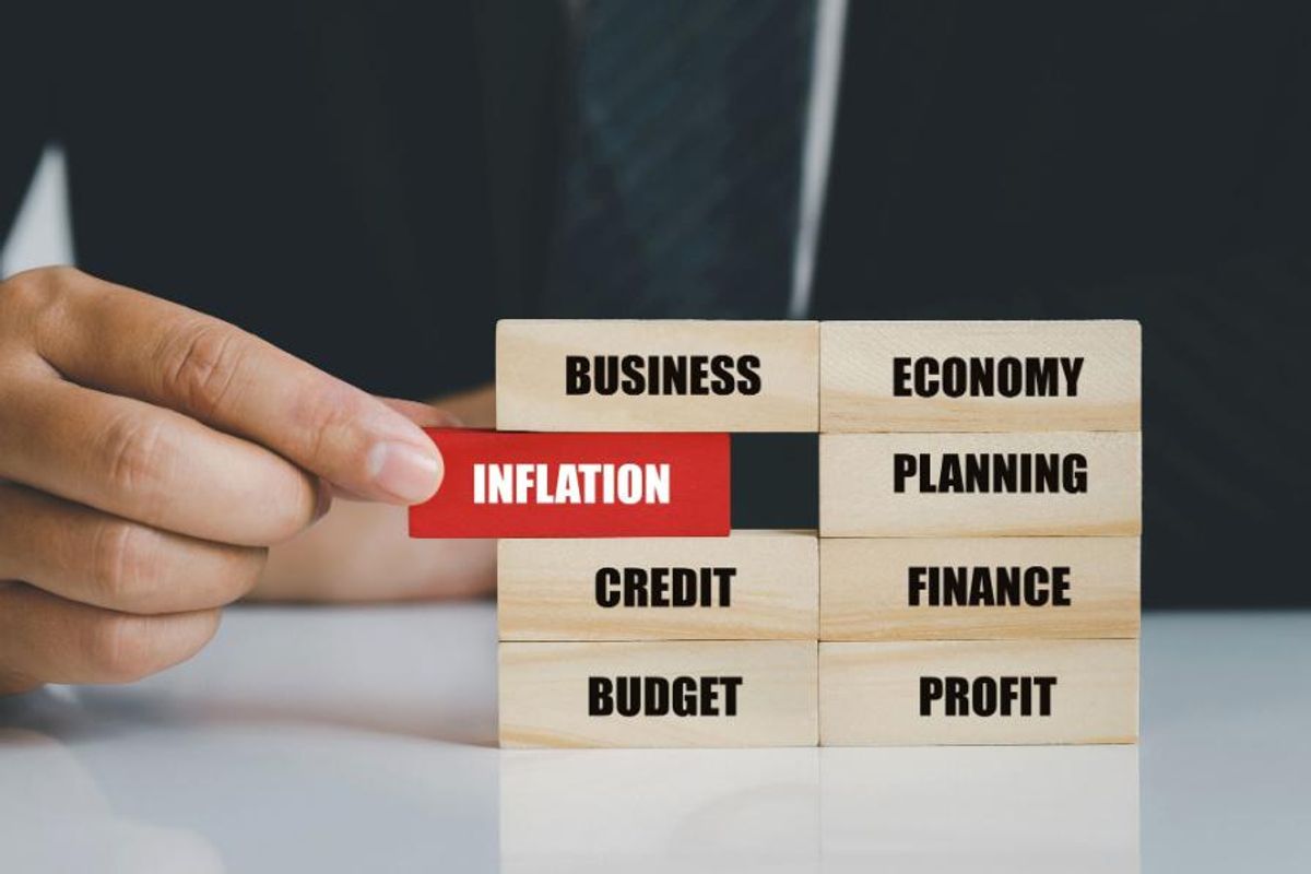 man holds wooden block with the word "inflation" written on it