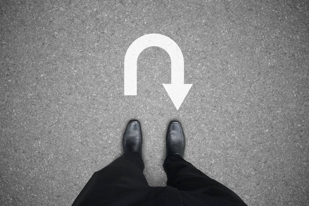 Man in black shoes standing on a road with a white U-turn arrow.