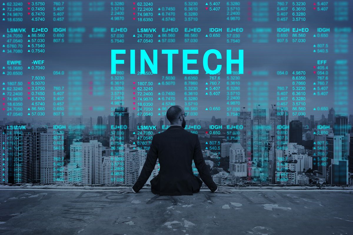 Man in suit sitting in front of the word "FINTECH" and digital financial numbers.