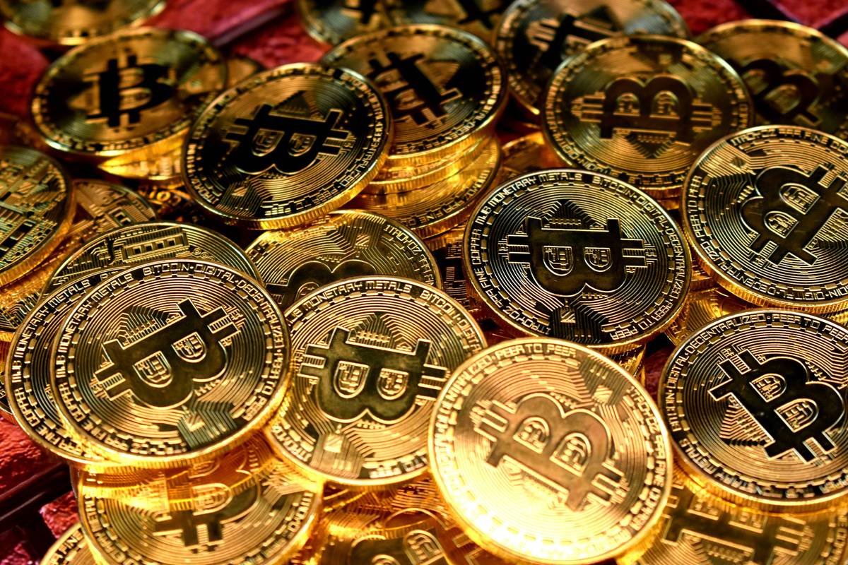 Many gold coins with Bitcoin symbols are stacked closely together, reflecting light.