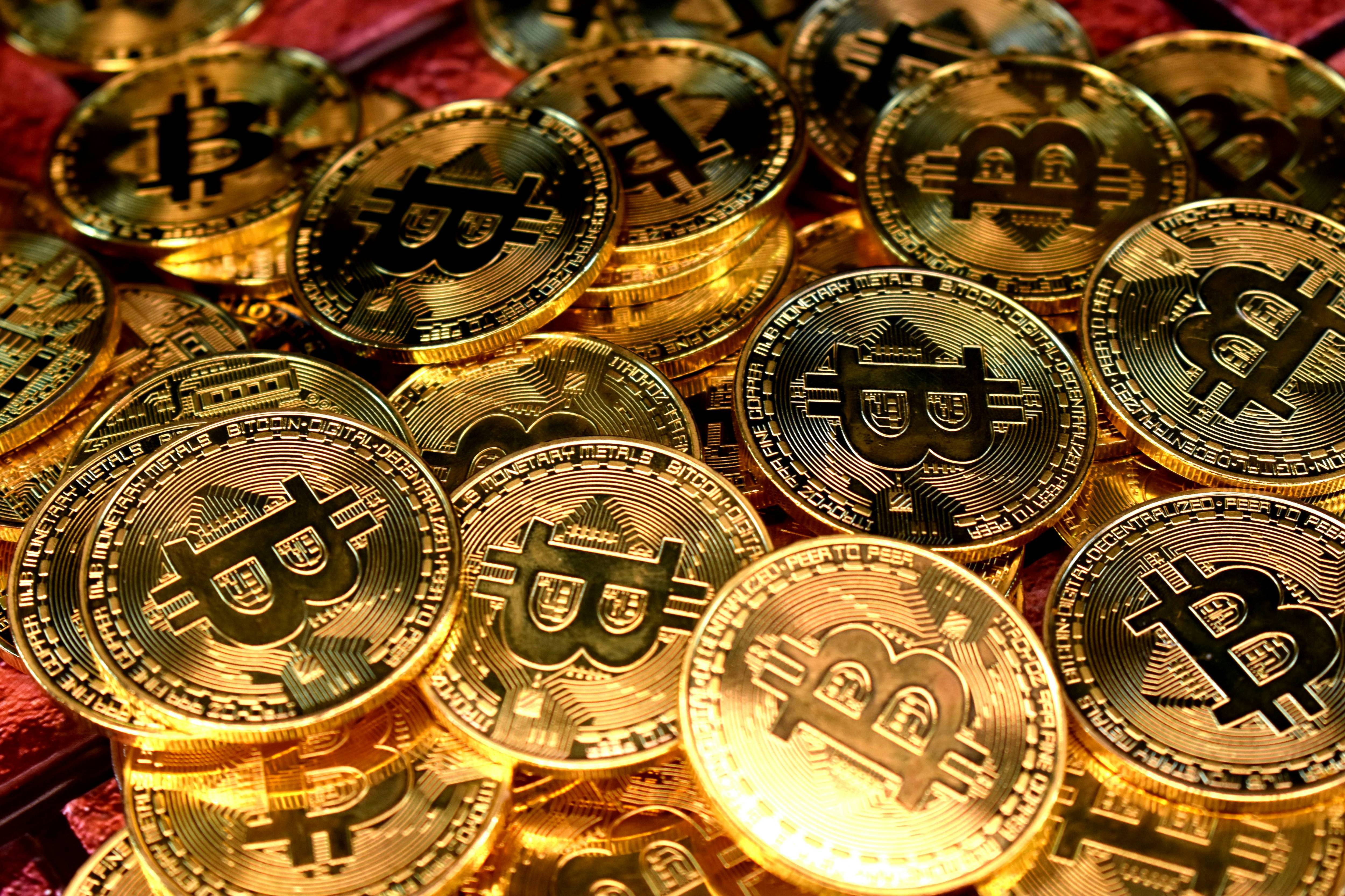 Many gold coins with Bitcoin symbols are stacked closely together, reflecting light.