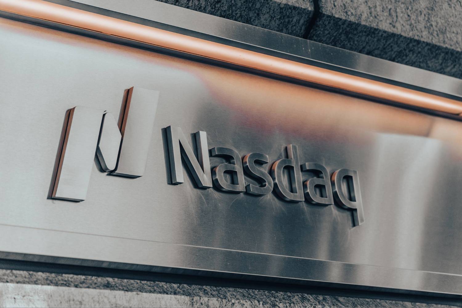 Metallic wall featuring embossed "Nasdaq" logo with stylized bars against a textured stone background.