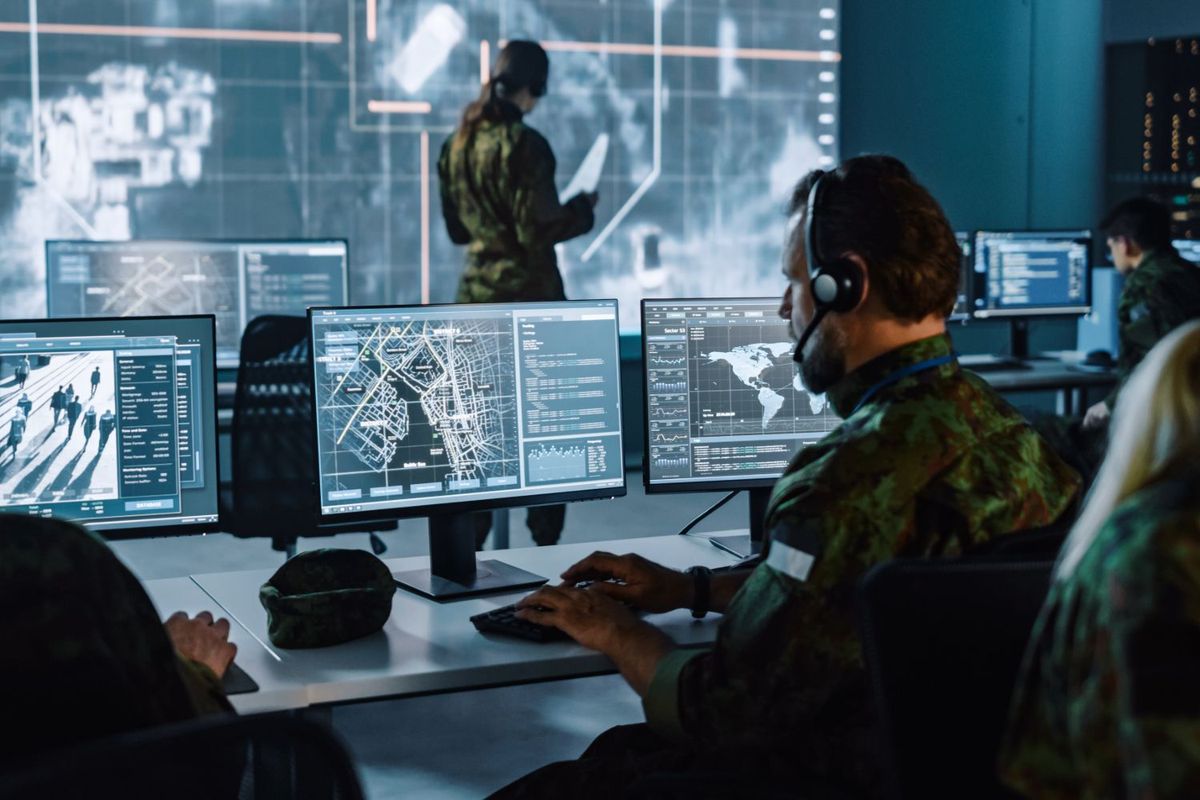 Military personnel using computers in a command center with maps and data on screens.