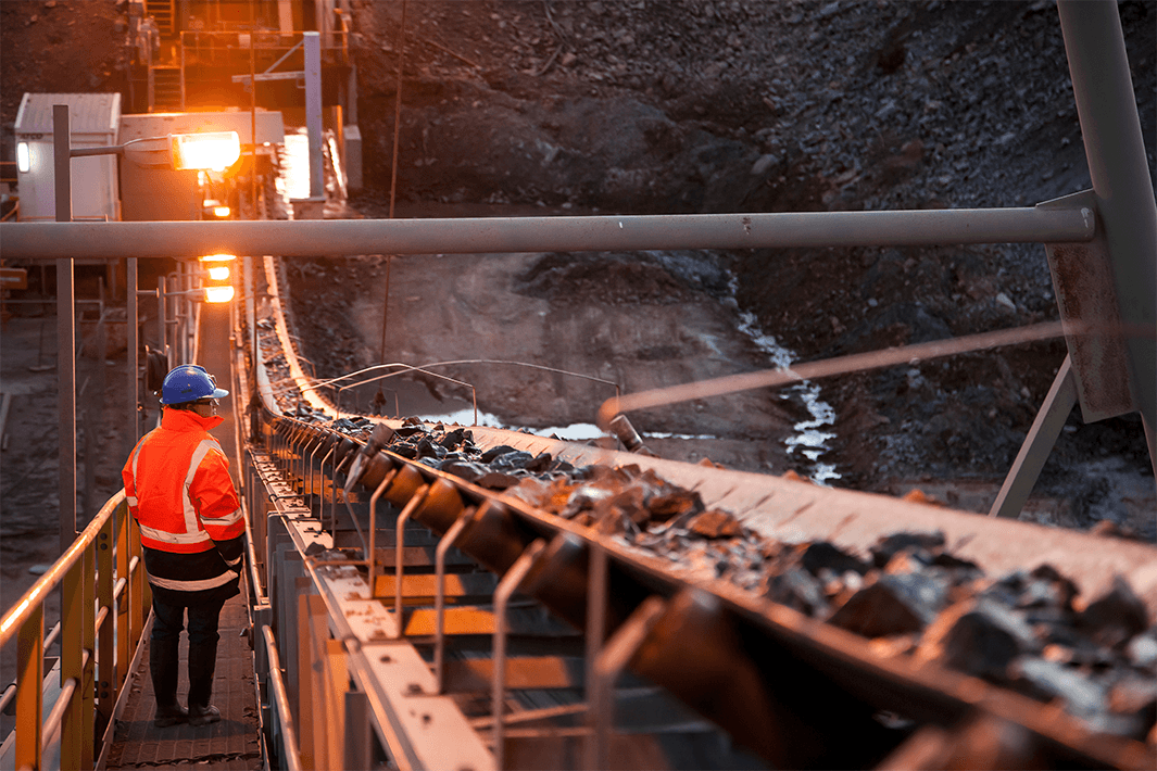 Miner inspecting ore rocks on a conveyor in New South Wales, Australia.