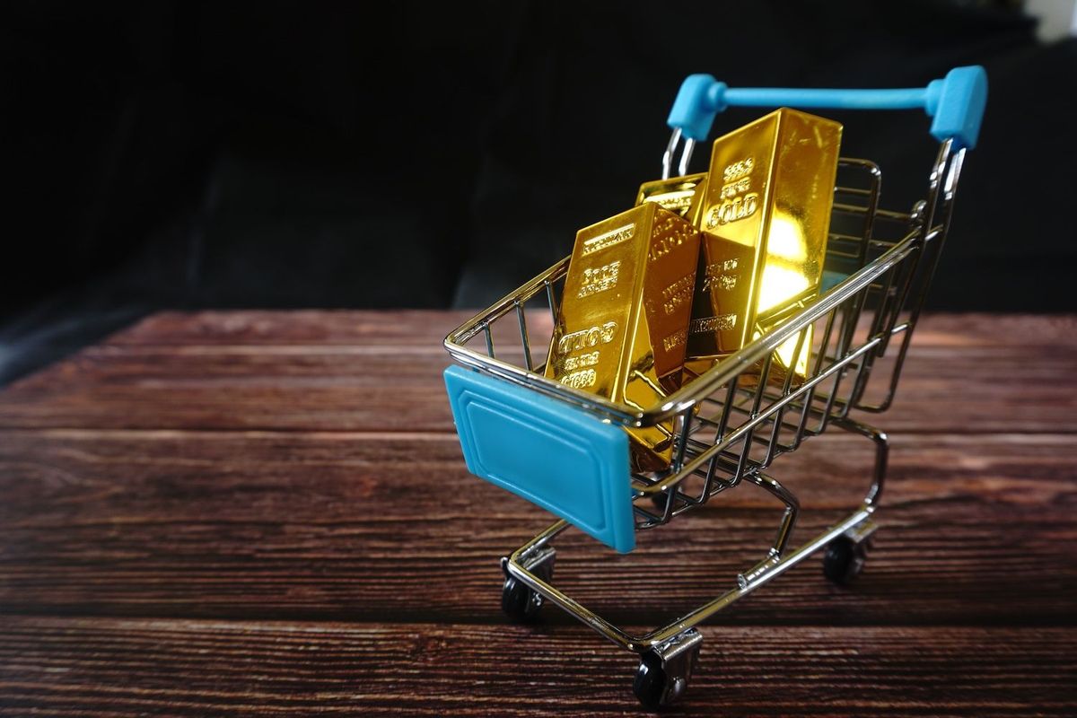 Mini cart with gold bars on wooden surface, dark background.