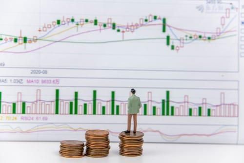 miniature man standing on stack of coins in front of bar graph