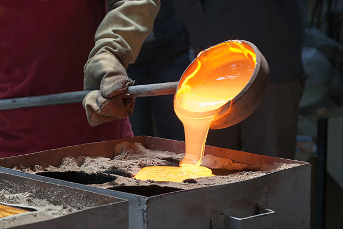 Molten metal being poured into a mold by a worker wearing heat-resistant gloves.