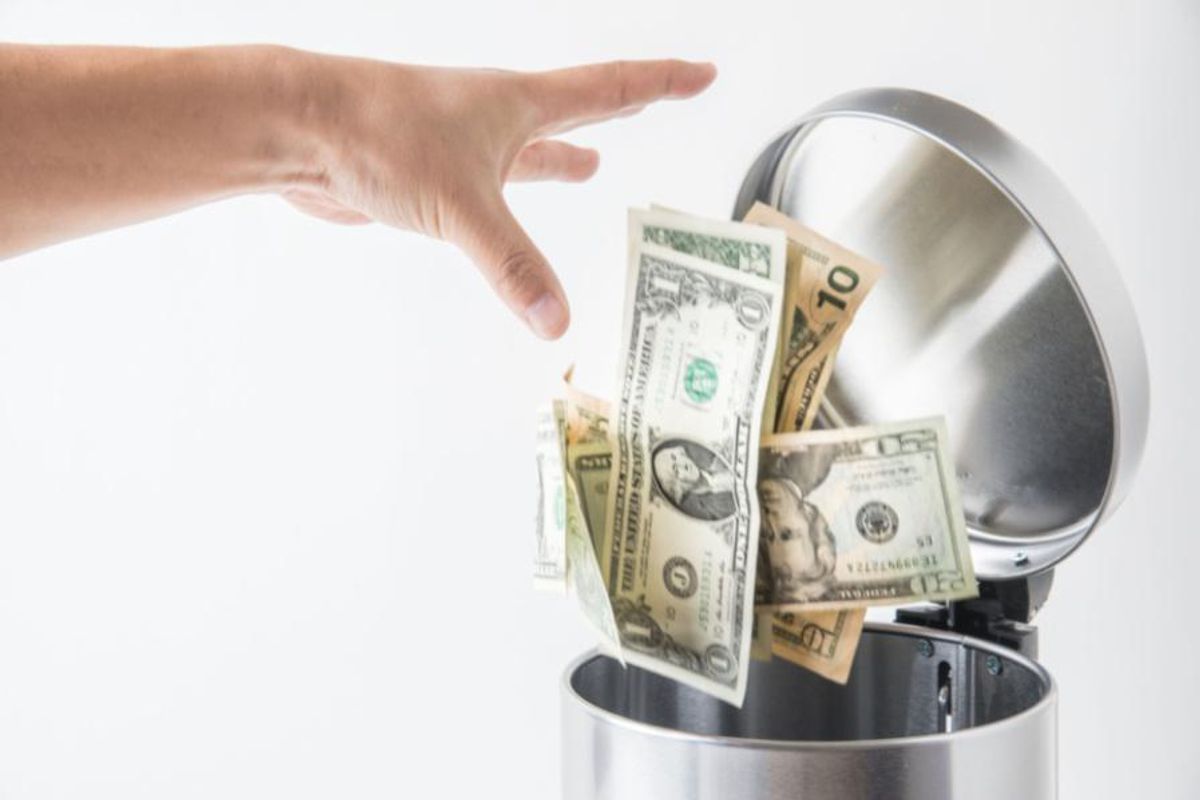money being thrown away in a wastebasket