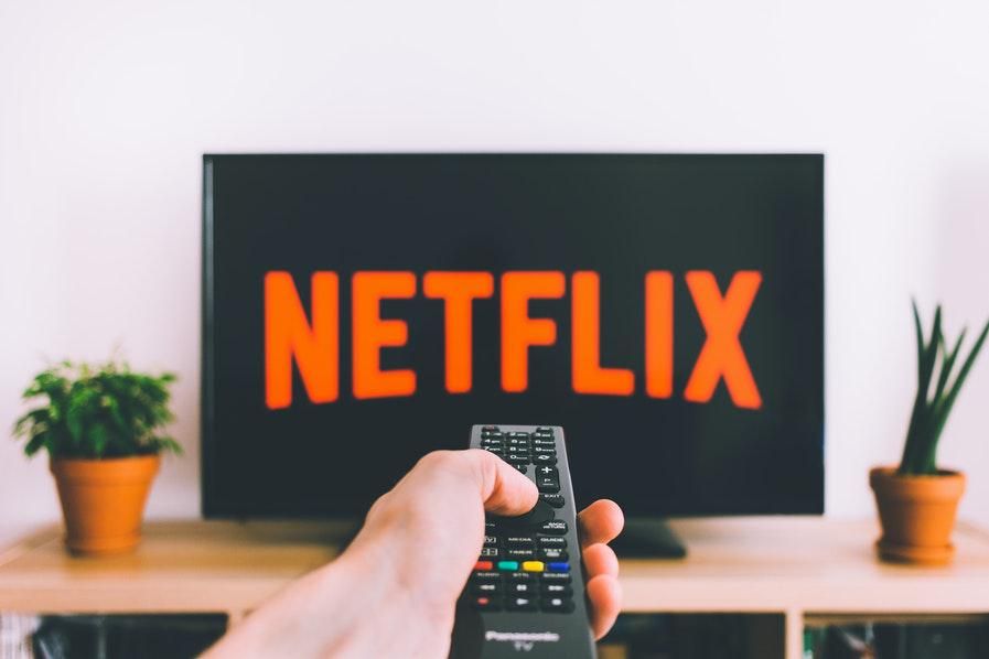 netflix logo displaying on a TV with someone pointing a remote at the screen
