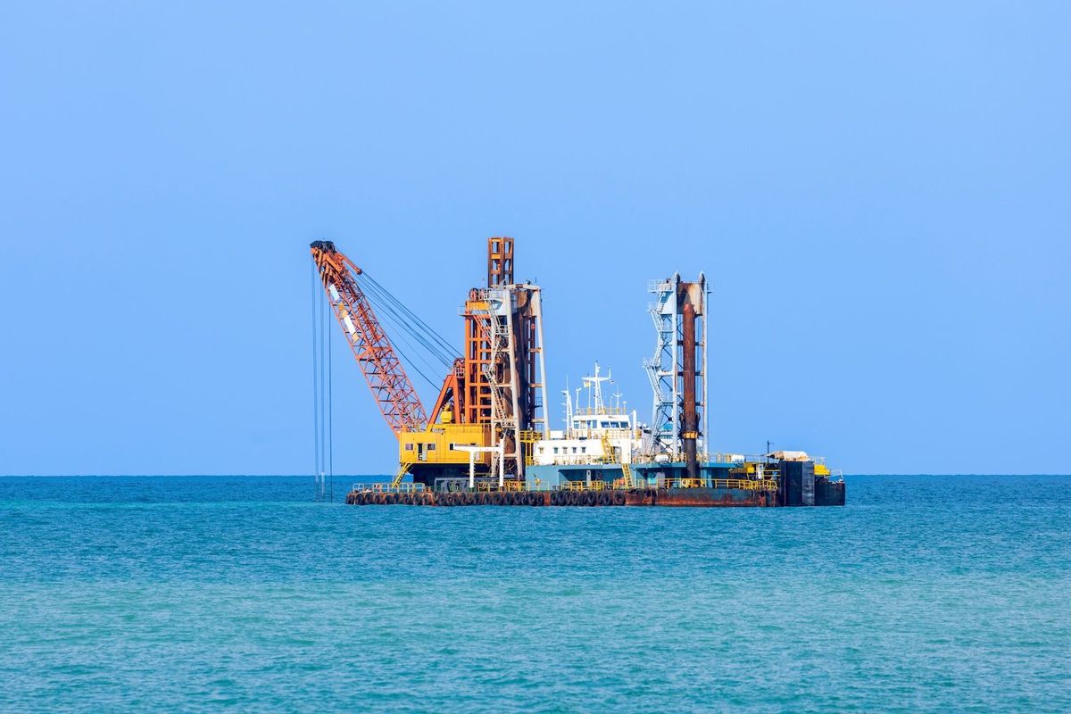 Offshore construction platform with cranes on calm blue sea.