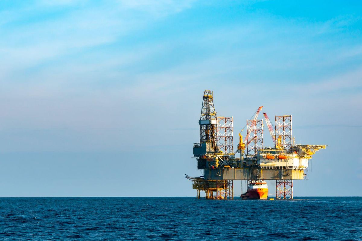 Offshore oil rig with support vessel under a bright blue sky.