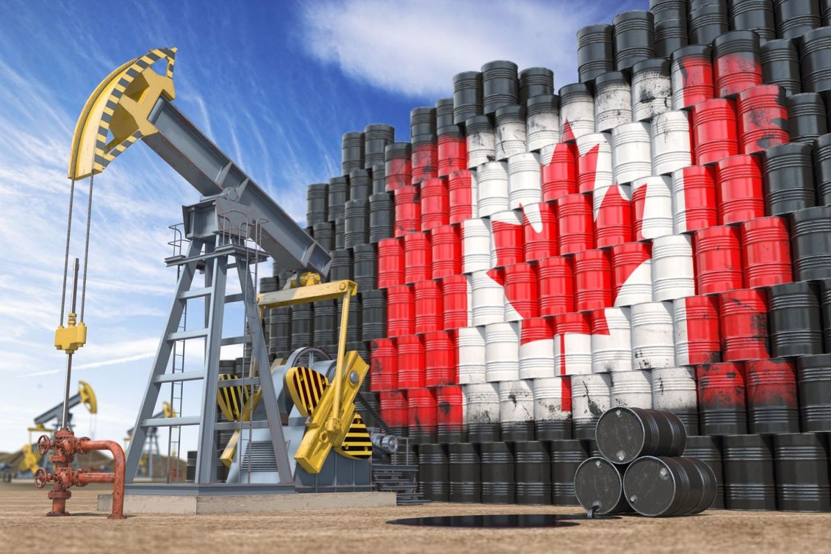 Oil rig in front of stacks of oil barrels with Canadian flag spray painted on them.