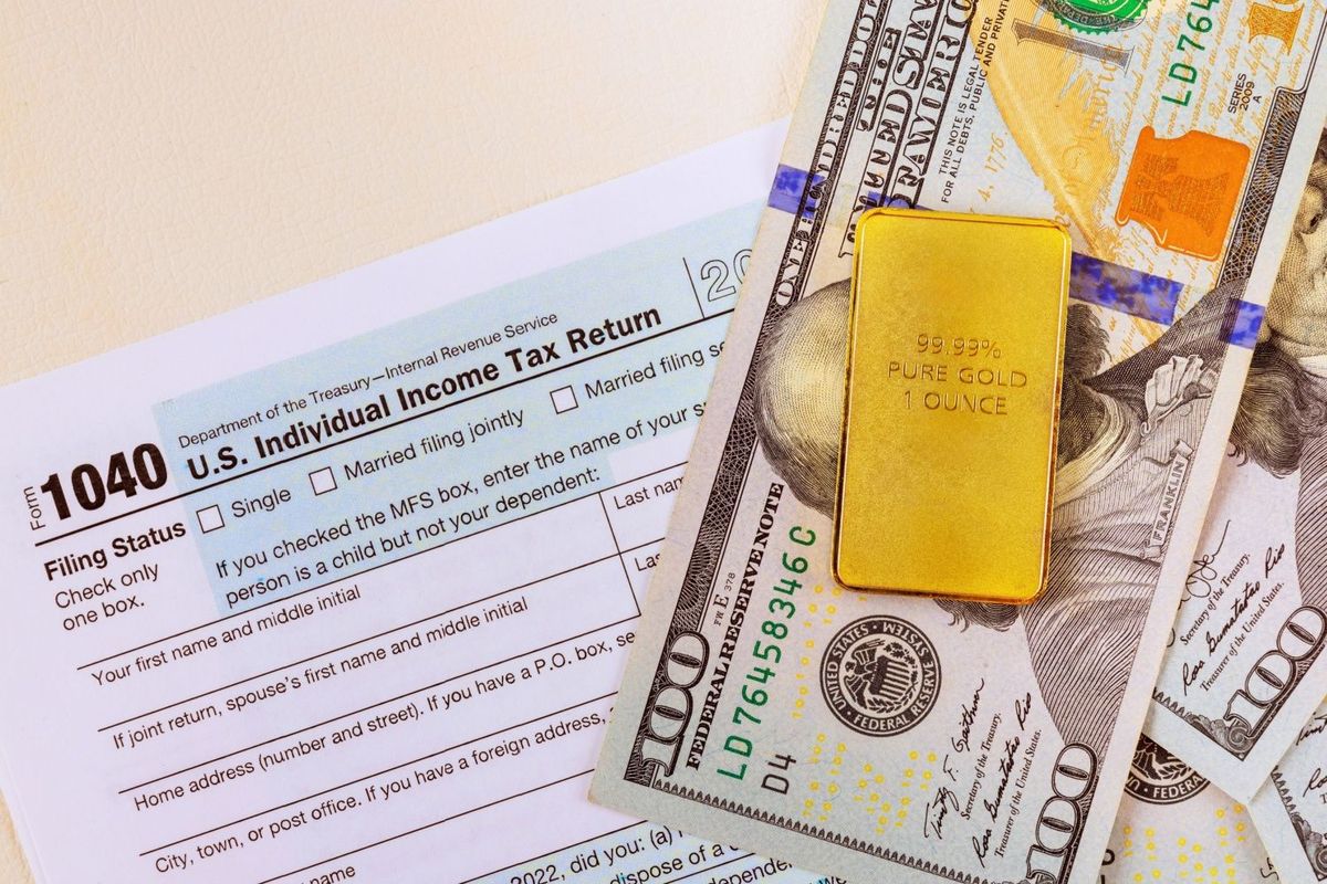 One ounce gold bullion bar on top of US$100 bill and Tax Form 1040.