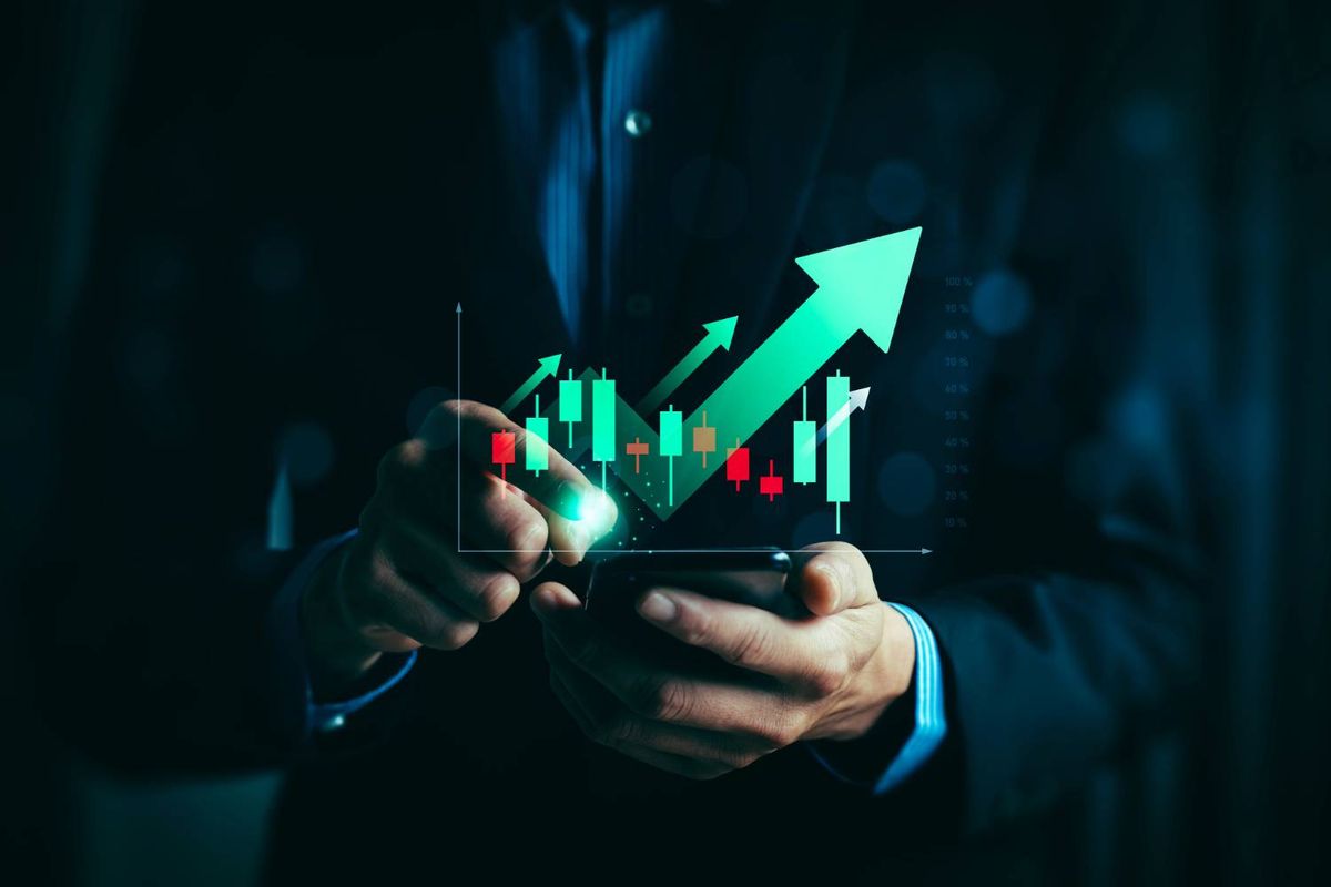Person analyzing stock chart with green upward arrows on a digital device.