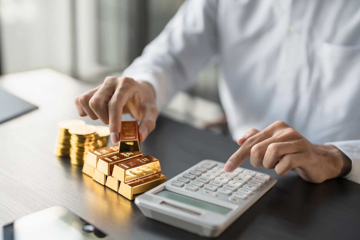 Person calculating with gold bars and coins on a table.