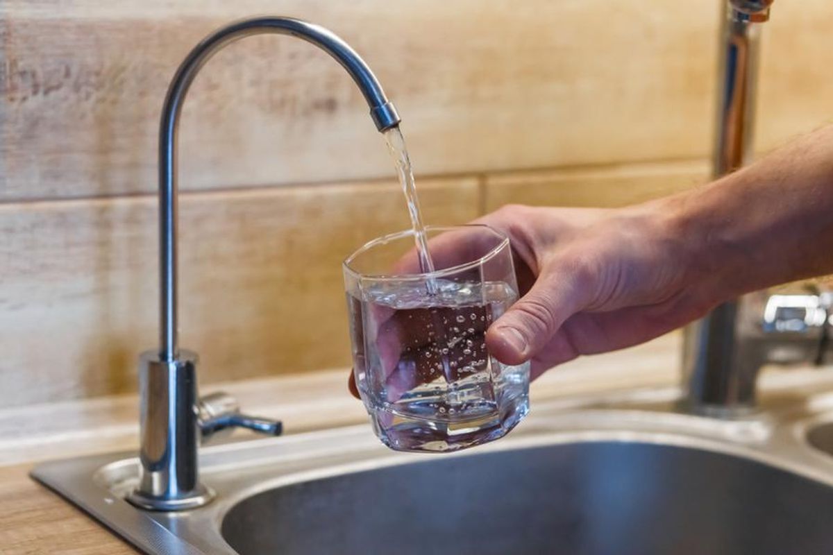 person fills up glass of clear water at sink
