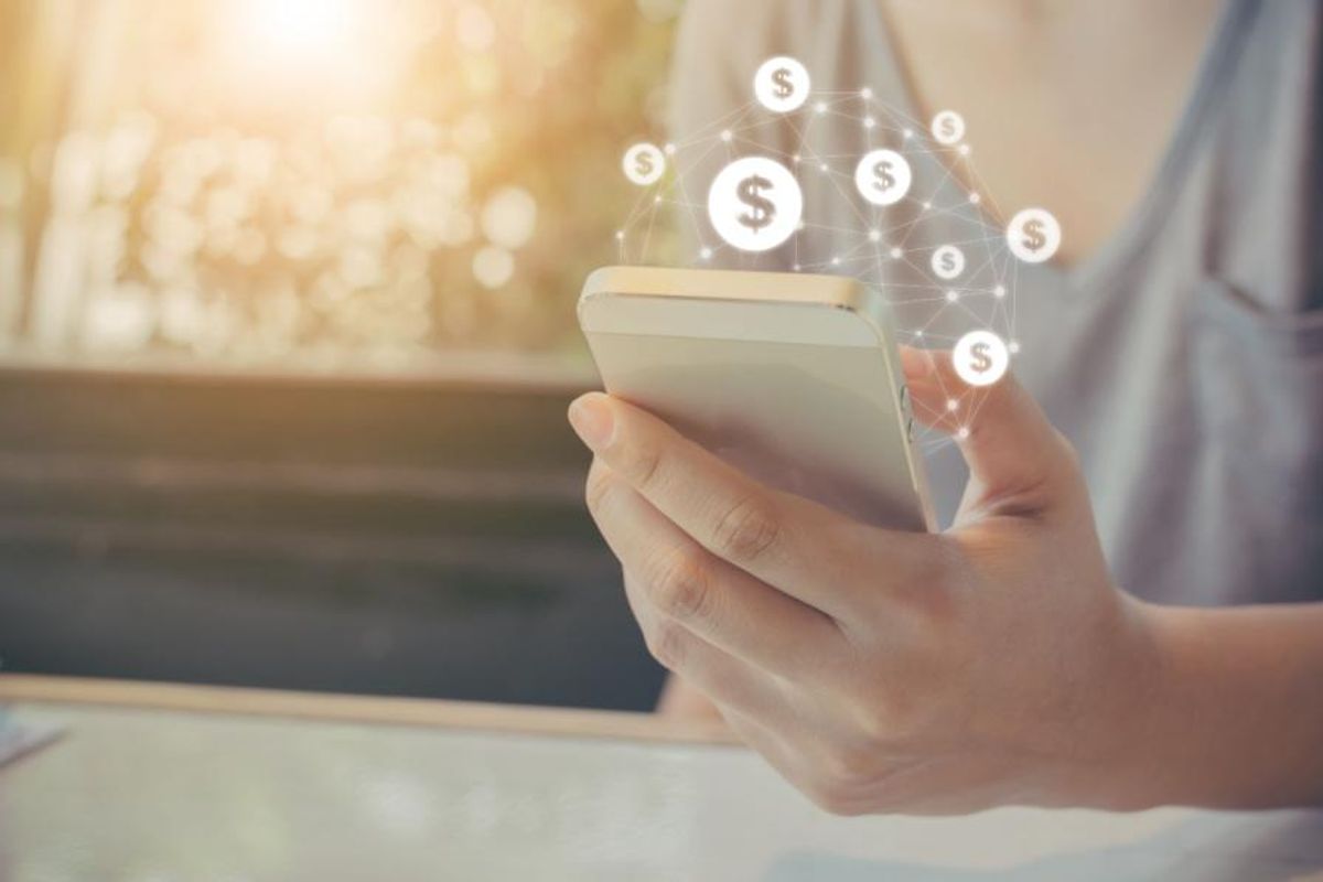 person holding cell phone with graphics showing dollar signs in front of the screen